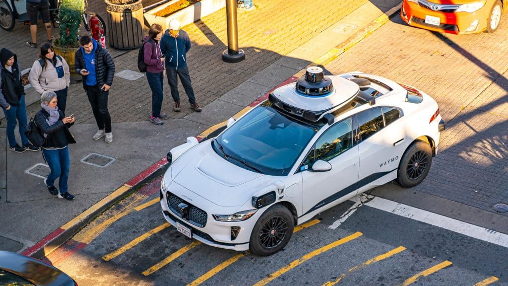 Carro da Waymo na rua com pedestres perto