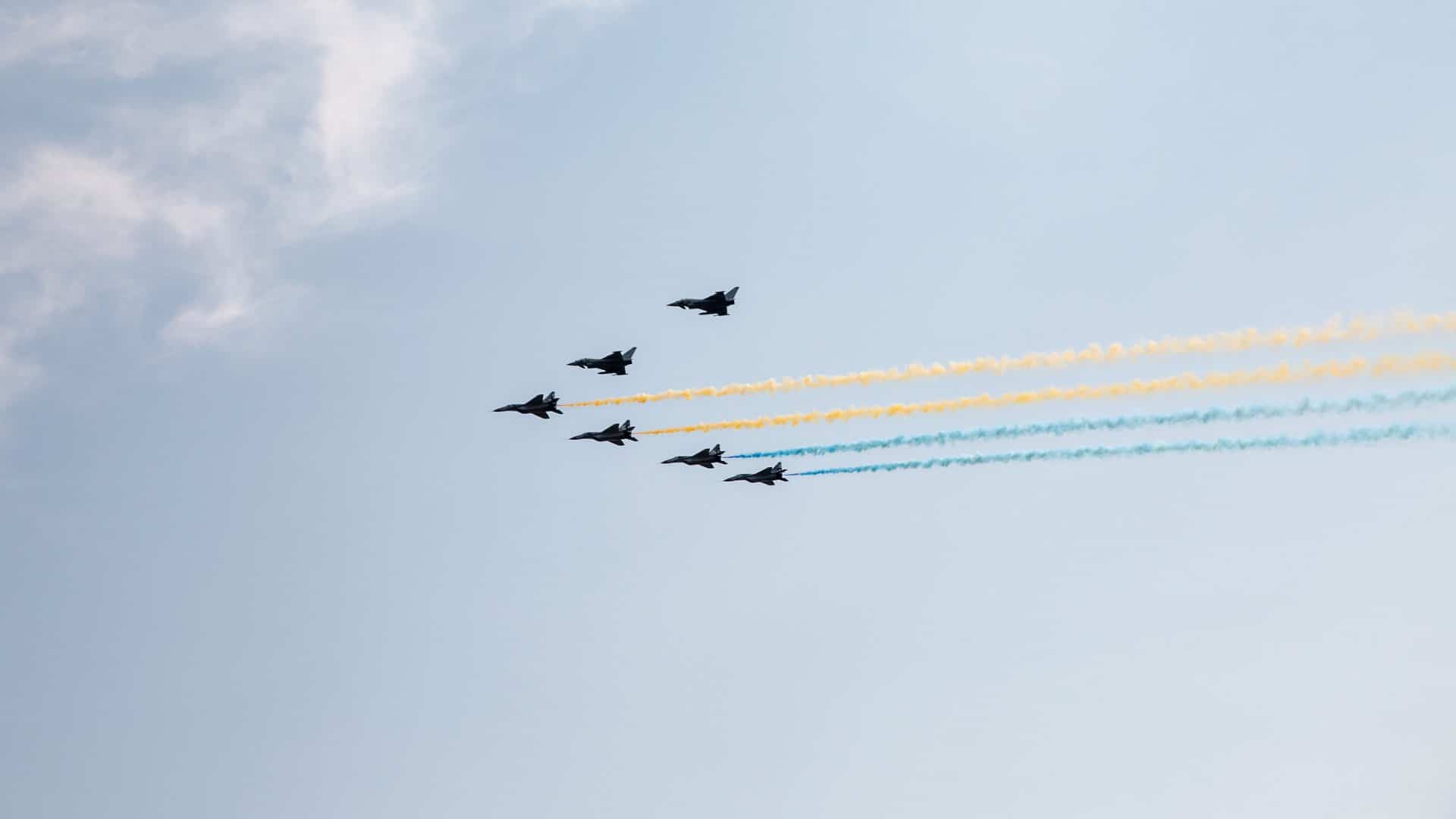 Seis caças F-16 voando em formação V soltando fumaça azul e amarela homenageando a Ucrânia