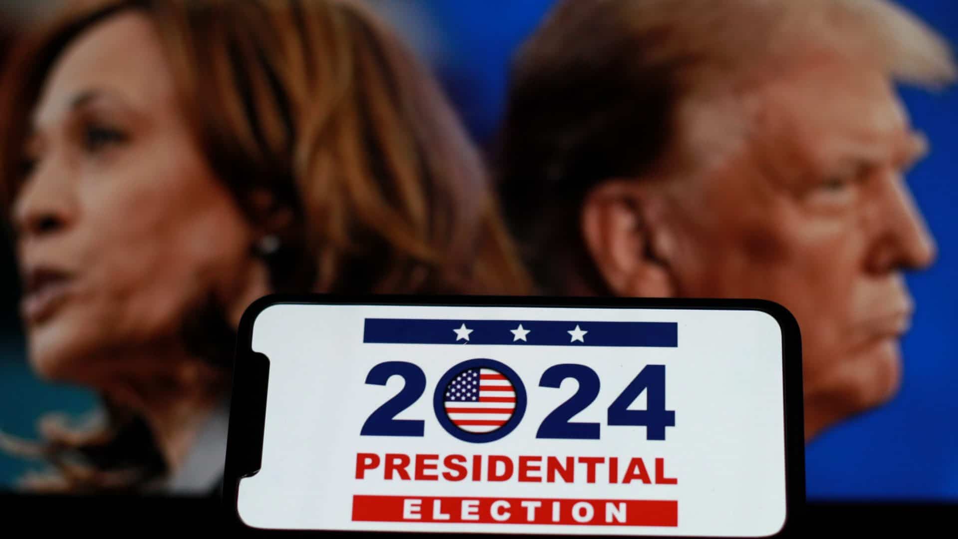 Celular com imagem sobre eleições presidenciais de 2024 dos Estados Unidos com foto de Kamala Harris e Donald Trump ao fundo