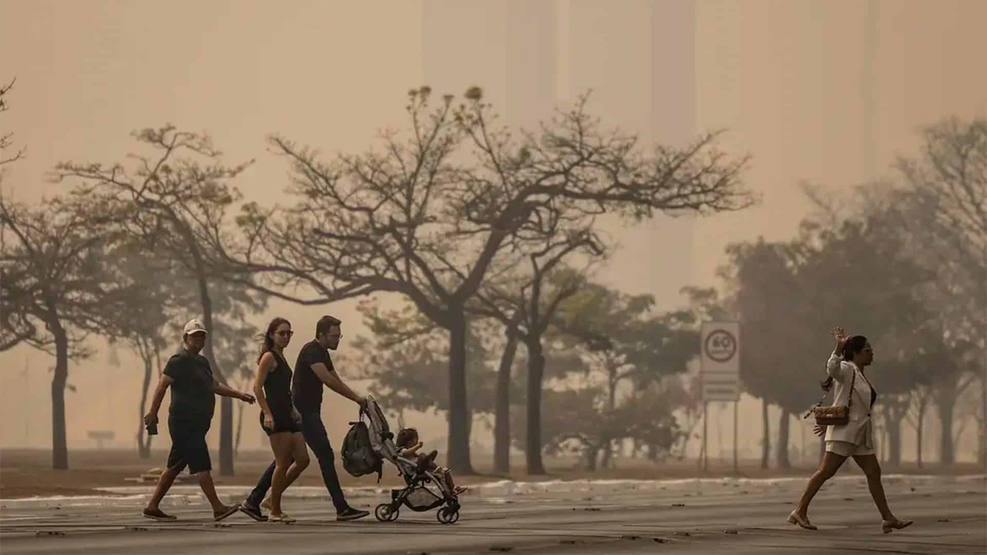 Pessoas andando na rua de uma cidade encoberta por fumaça de queimadas
