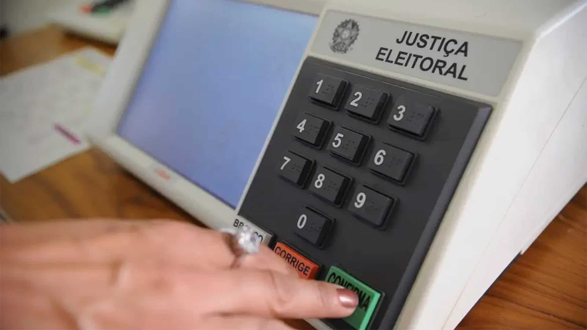 Mulher apertando botão verde de confirma em urna eletrônica brasileira