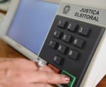 Mulher apertando botão verde de confirma em urna eletrônica brasileira