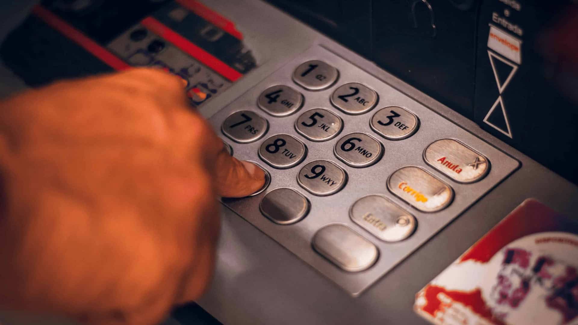 Pessoa digitando senha no teclado de um caixa eletrônico para sacar dinheiro