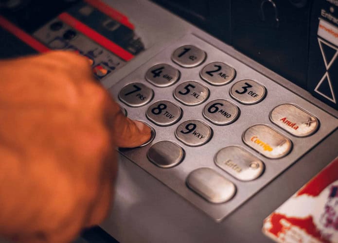 Pessoa digitando senha no teclado de um caixa eletrônico para sacar dinheiro