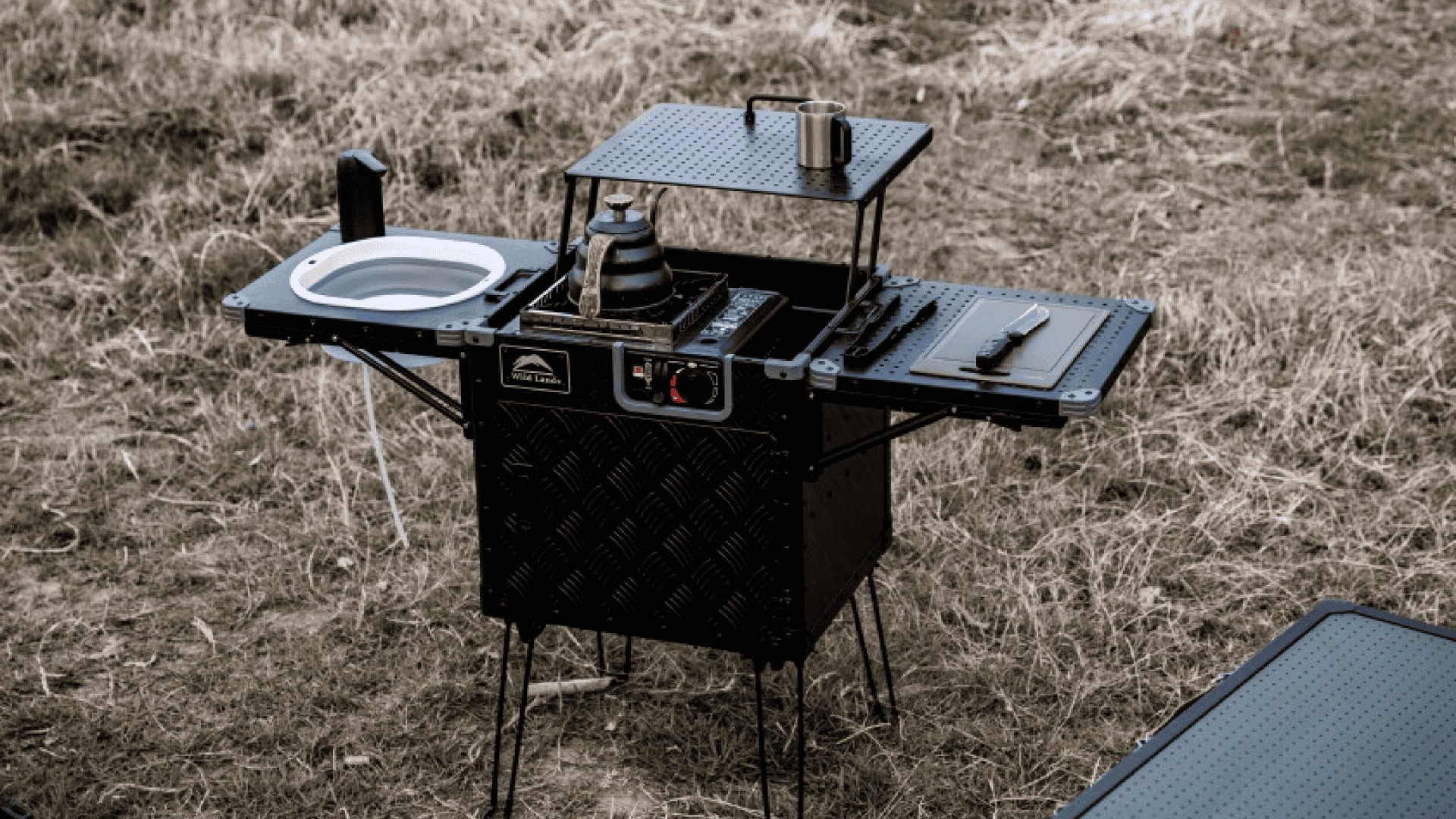 Imagem mostra uma cozinha portátil ao ar livre, no chão de grama
