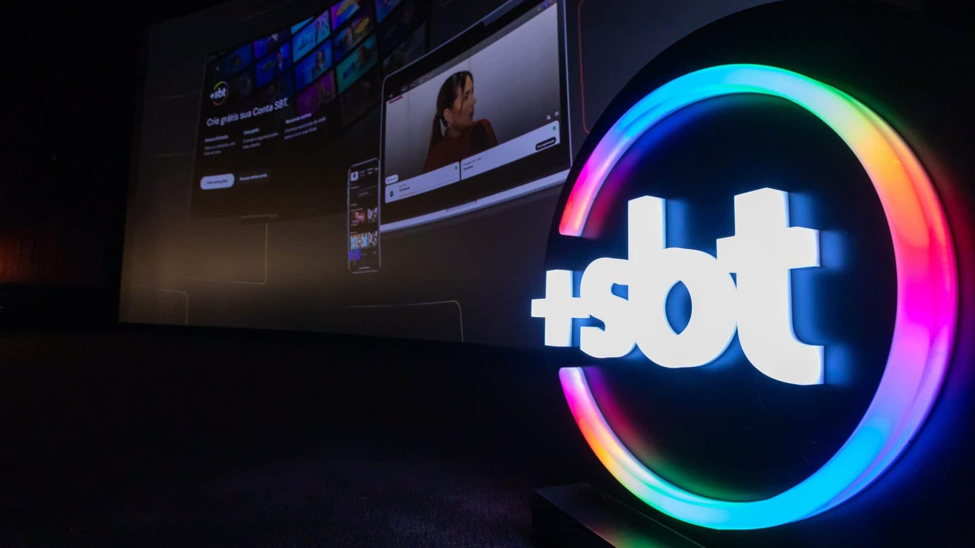 Logo do +SBT, com conteúdos do streaming ao fundo