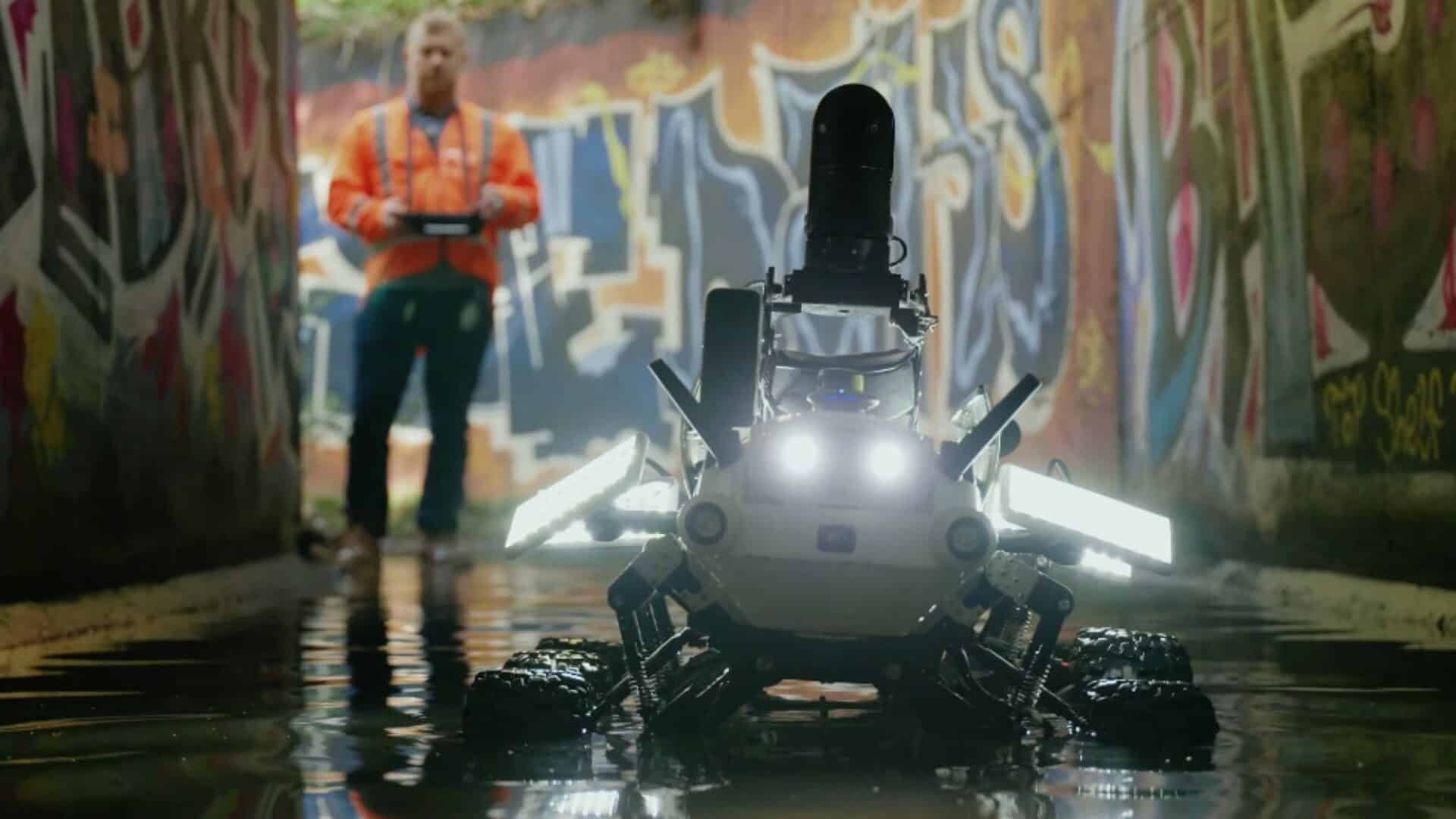 Robô aparece no esgoto, com uma pessoa atrás dele, controlando-o