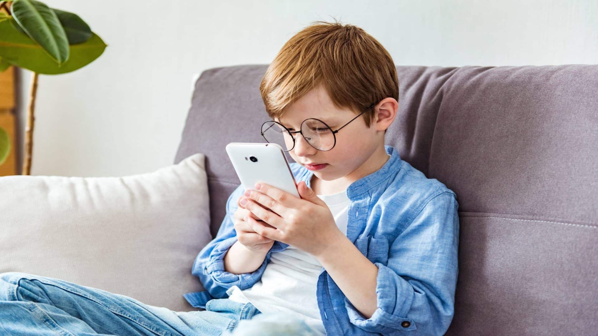 Menino de óculos brinca com o tablet. Conceito de vista ruim, malefícios dos gadgets, miopia.