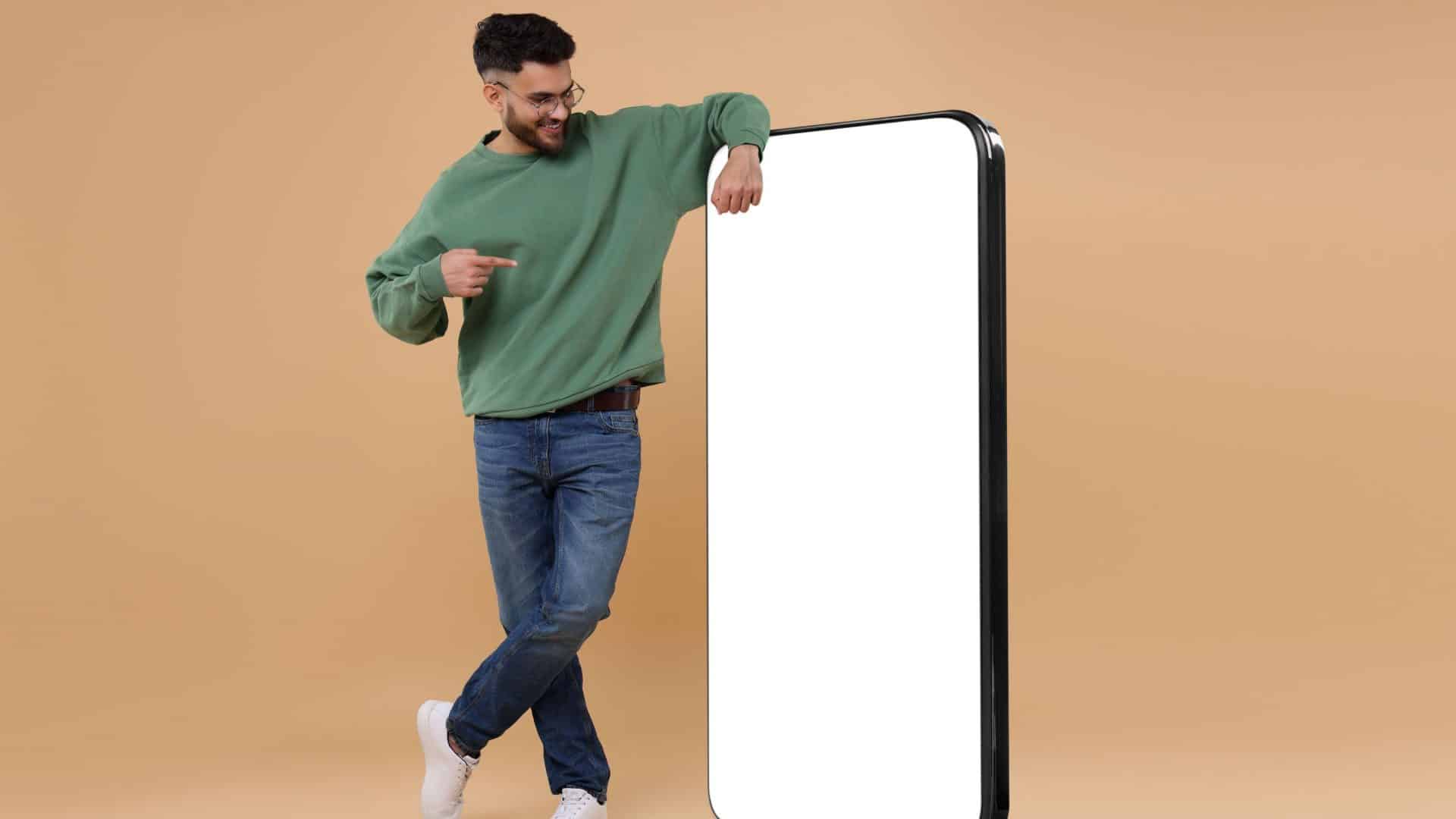 Homem apontando para um enorme celular com a tela vazia em um fundo bege escuro. Mockup para design.