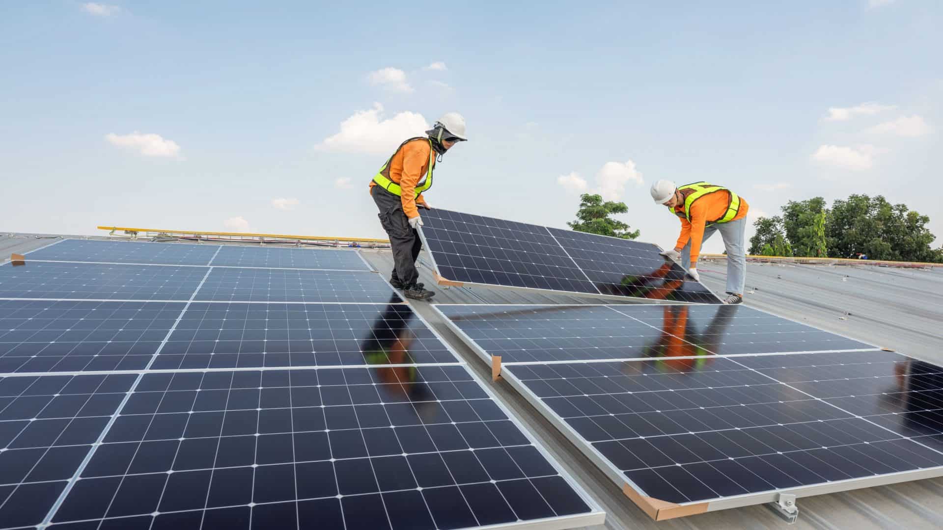 Técnicos transportando módulos solares fotovoltaicos no telhado da fábrica de manhã. Instalando uma célula solar no telhado. Painéis solares no telhado. Operários instalando uma usina de energia solar, tecnologia ecológica.