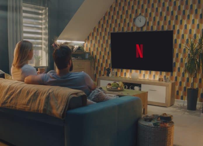 ZAPORIZHYA, UCRÂNIA - 7 DE JUNHO DE 2024: Casal bebe chá e começa a assistir filme ou programa de TV no serviço de streaming Netflix sentado no sofá em casa e descansando. Logotipo da Netflix exibido na grande tela da TV
