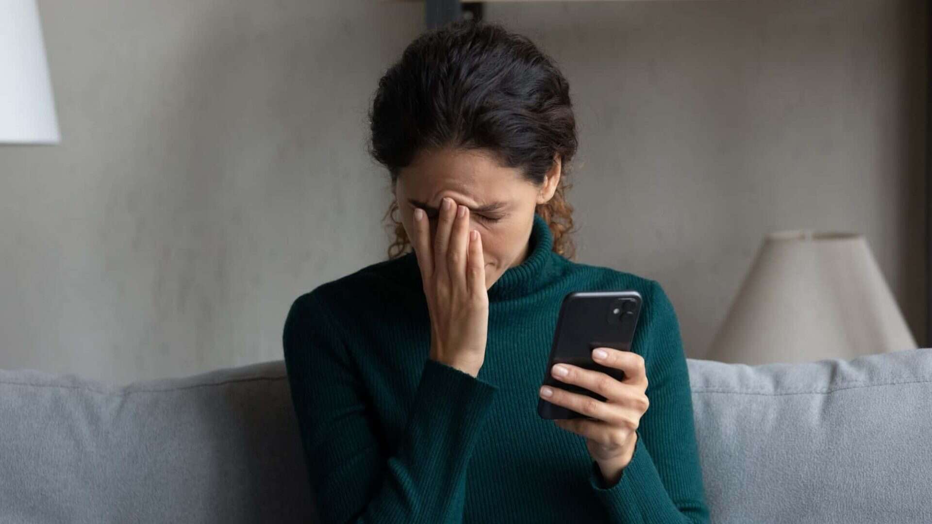 Mulher com mão no rosto e expressão preocupada enquanto segura celular