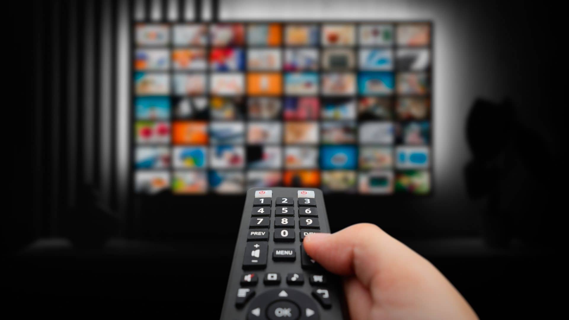 Pessoa apontando controle para TV com vários quadradinhos de programas na tela
