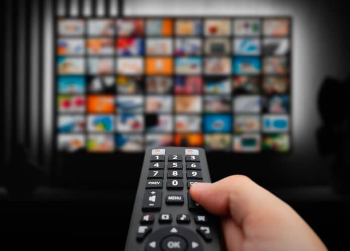 Pessoa apontando controle para TV com vários quadradinhos de programas na tela