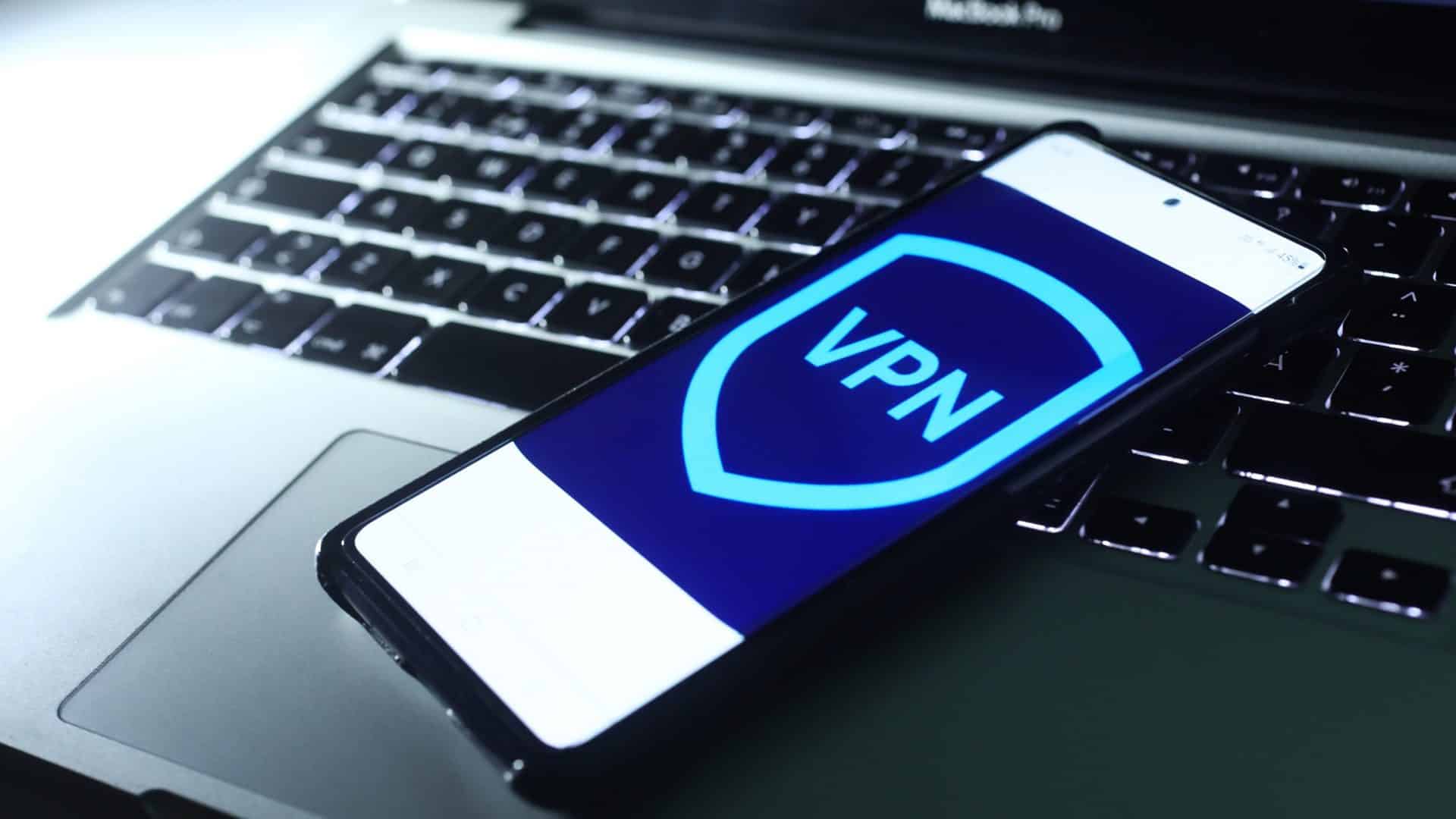 Imagem de um logo de VPN em um smartphone, que está em cima de um notebook