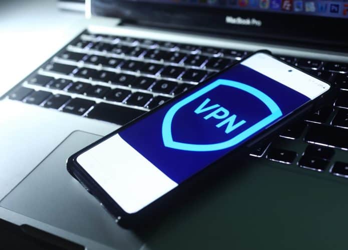 Imagem de um logo de VPN em um smartphone, que está em cima de um notebook