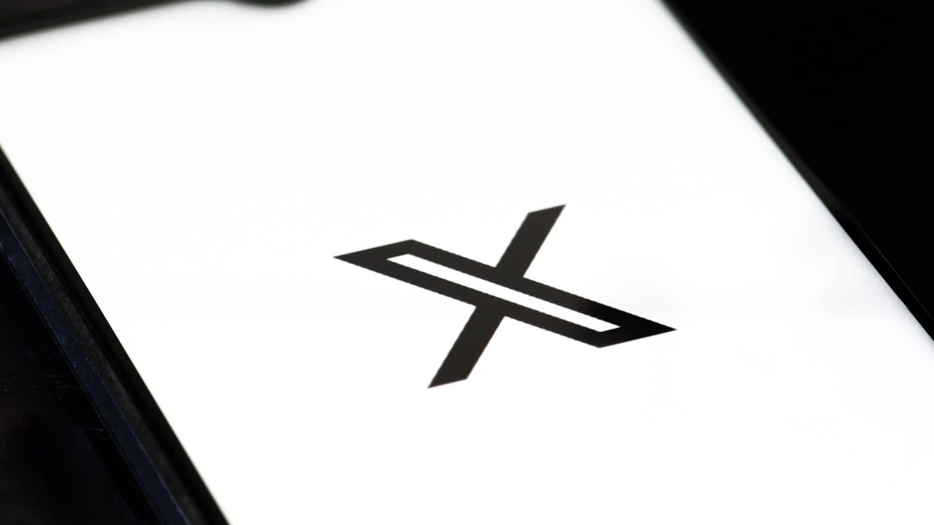 Logo do X, preto, em fundo branco, mostrado em um smartphone