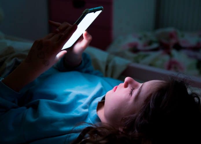 Garota usando celular na cama