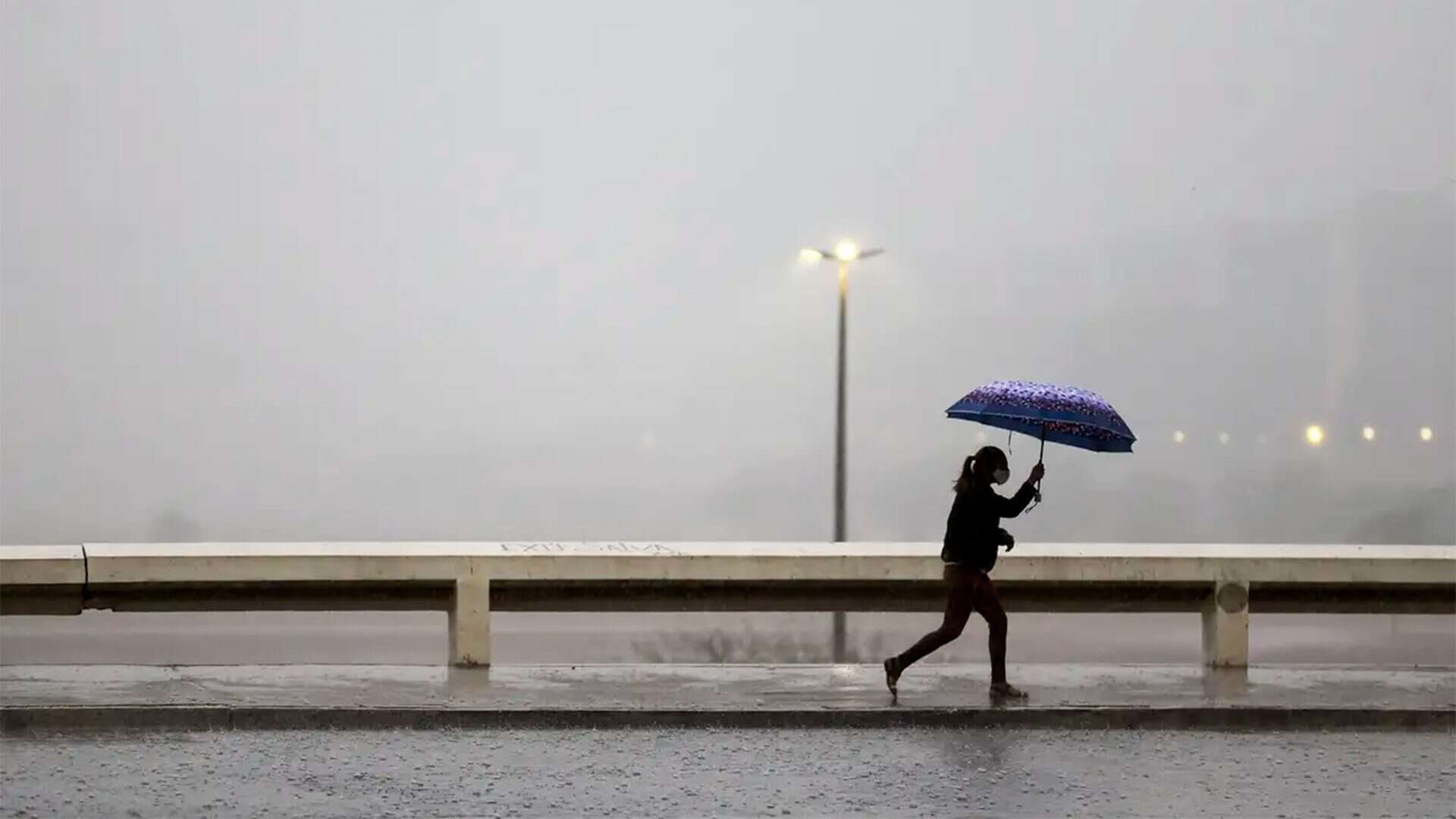 Mulher andando na chuva com guarda-chuva aberto