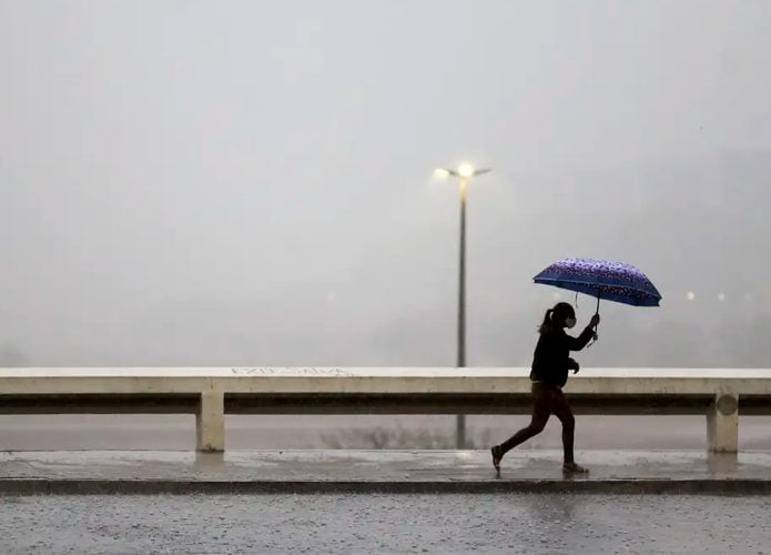 Mulher andando na chuva com guarda-chuva aberto