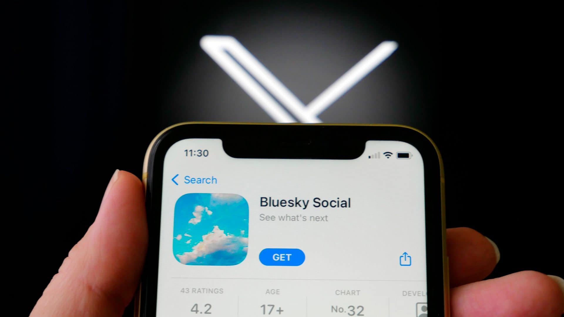 Pessoa segurando iPhone com página do Bluesky na App Store aberta e, ao fundo, logomarca do X (antigo Twitter)