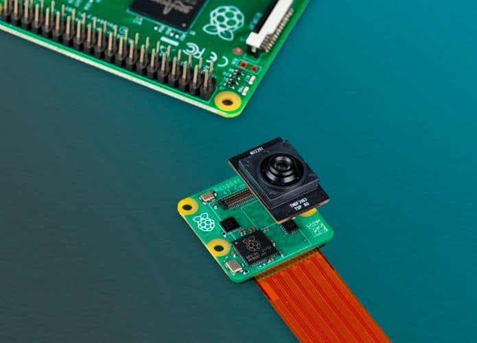 Camerazinha com IA da Raspberry Pi desenvolvida em parceria com a Sony ao lado de placa tecnológica da marca