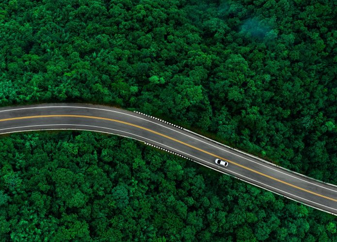 Visão aérea de carro elétrico andando em estrada que corta floresta