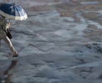 Mulher andando na com guarda-chuva aberto em dia com chuva e sol