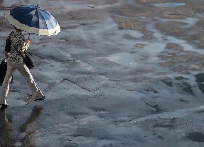 Mulher andando na com guarda-chuva aberto em dia com chuva e sol
