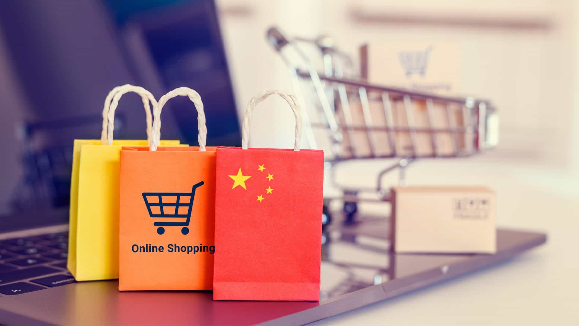 Miniaturas de sacolas com desenhos de compra on-line e bandeira da China colocadas na frente de miniatura de carrinho de mercado com caixas em cima de notebook