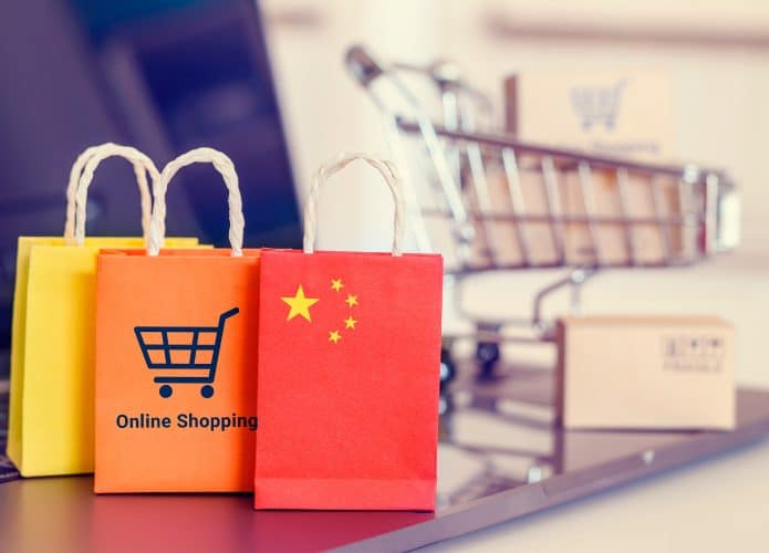 Miniaturas de sacolas com desenhos de compra on-line e bandeira da China colocadas na frente de miniatura de carrinho de mercado com caixas em cima de notebook