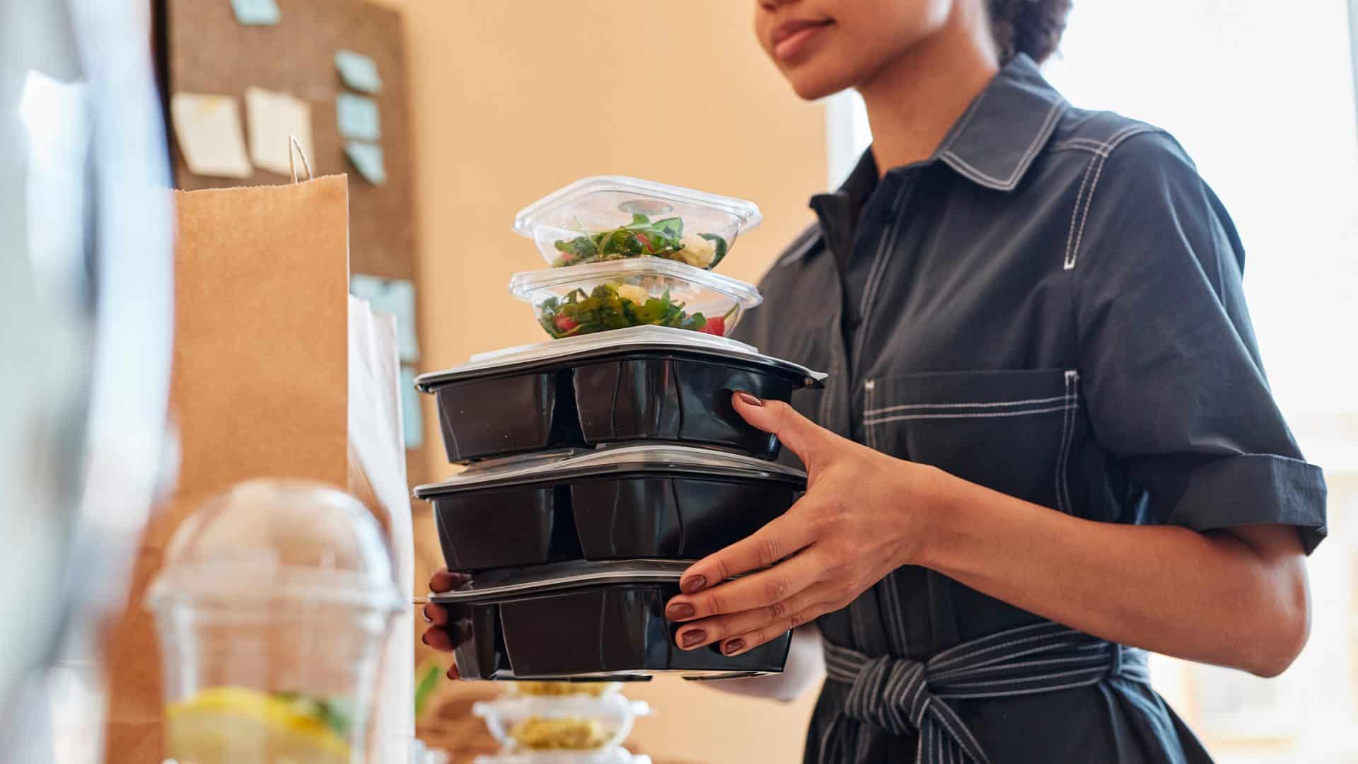 Mulher carregando três marmitas grandes e duas menores de plástico