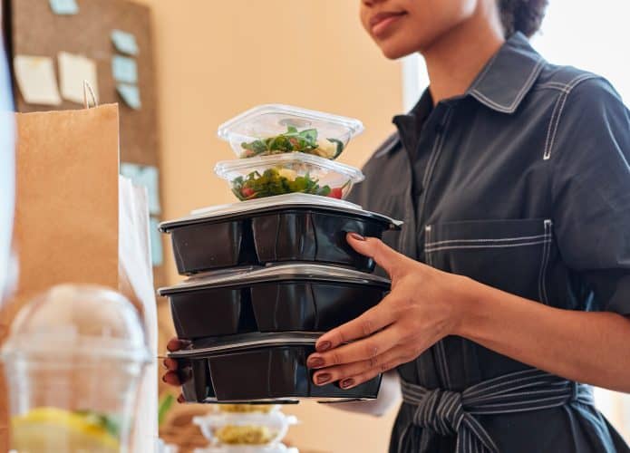 Mulher carregando três marmitas grandes e duas menores de plástico