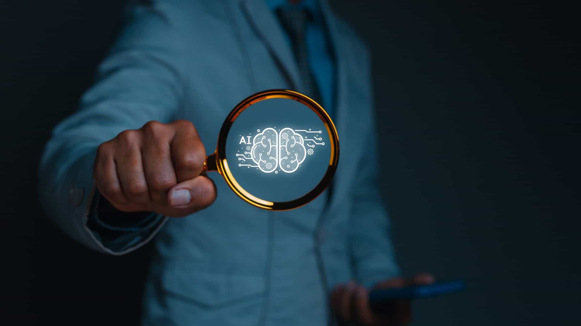 Pessoa segurando lupa com ilustração de cérebro e sigla de inteligência artificial