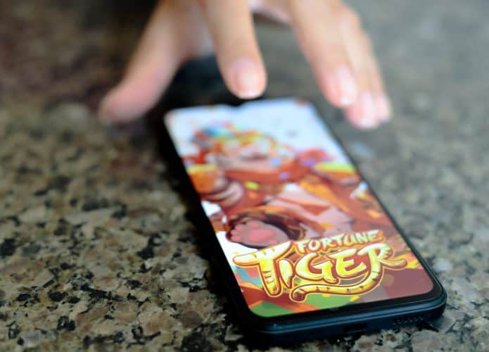 Mão estendida quase alcançando celular com jogo do tigrinho aberto