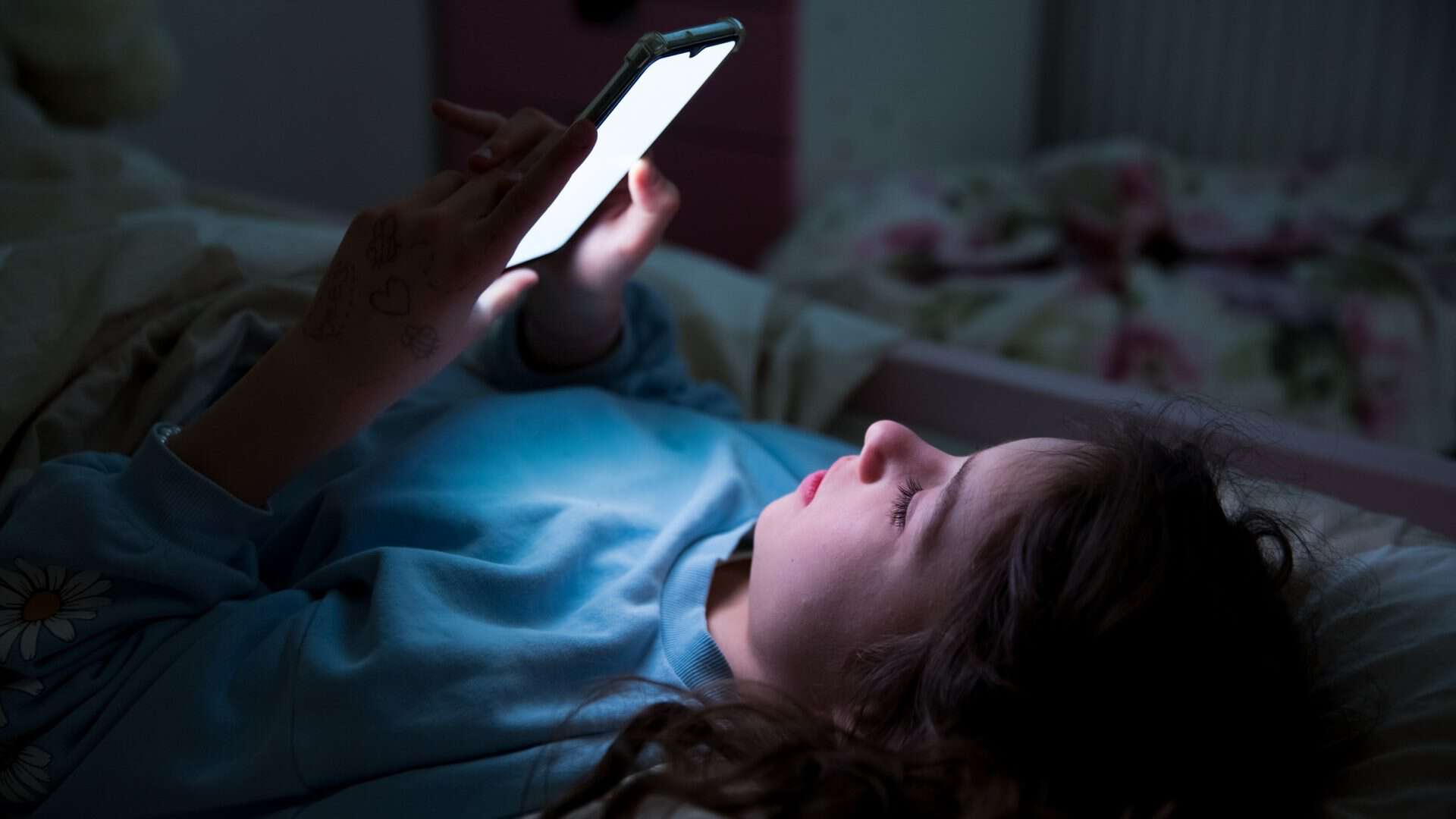 Criança deitada no escuro olhando um celular