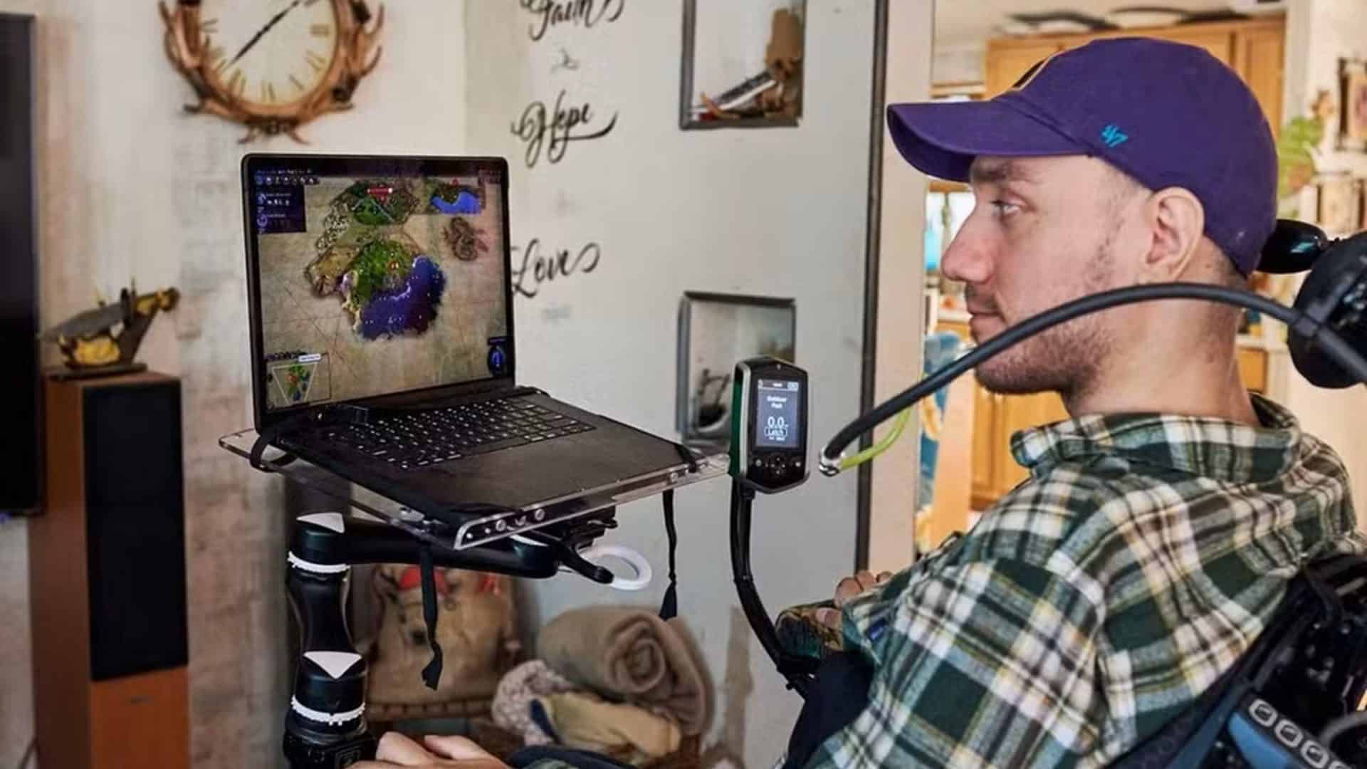 Noland Arbaugh sentado na cadeira rodas olhando para o notebook