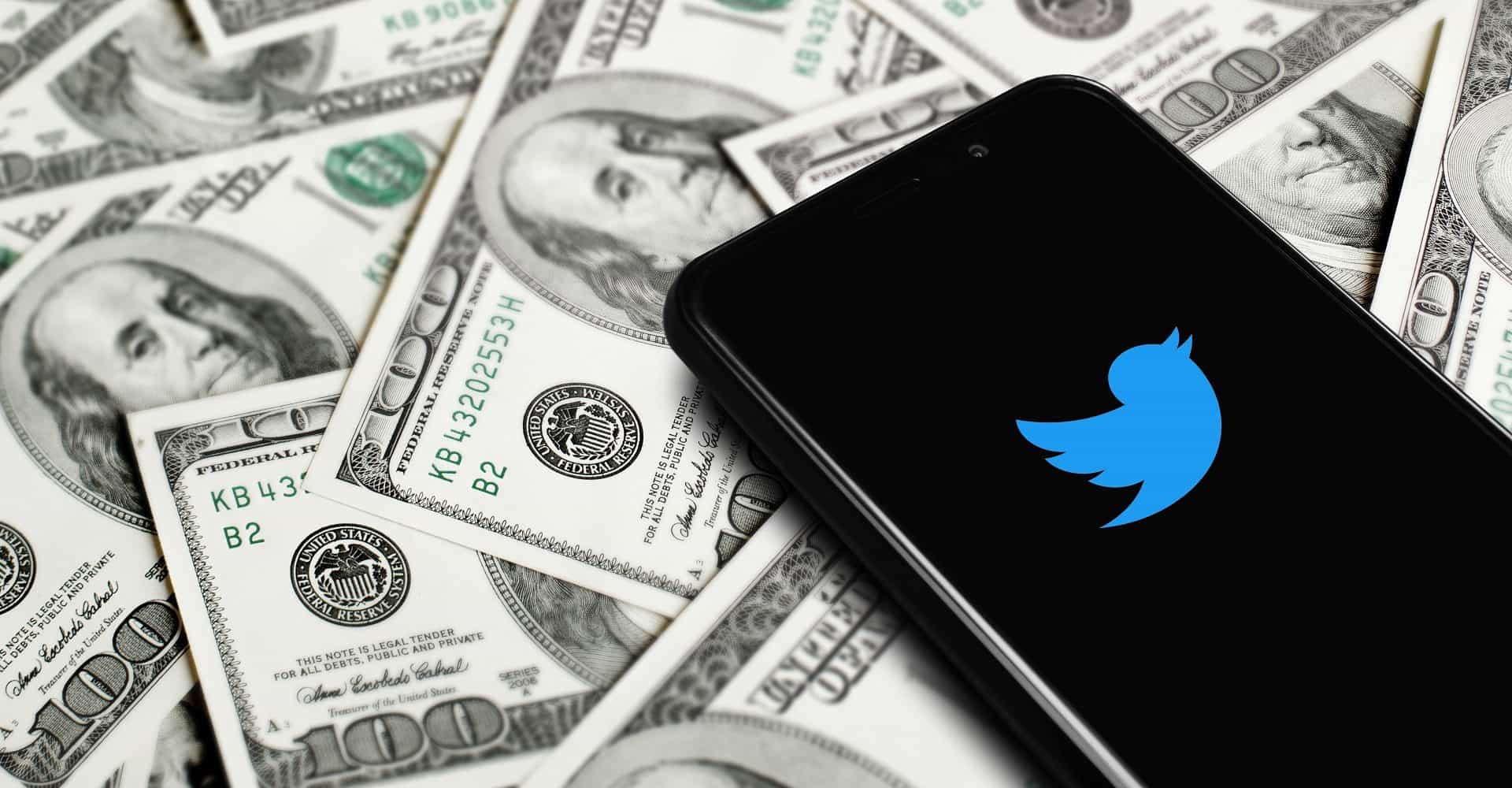 celular com o logo do Twitter cercado de notas de dólares