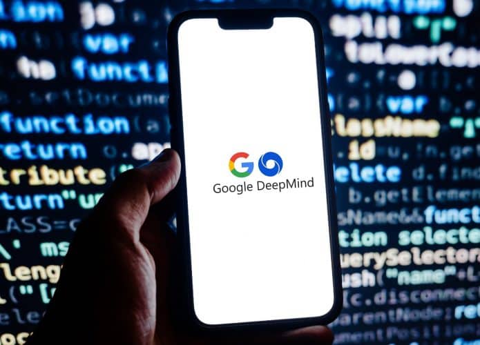 Pessoa segurando celular com logomarcas do Google e do DeepMind na tela, colocado na frente de tela exibindo códigos de programação