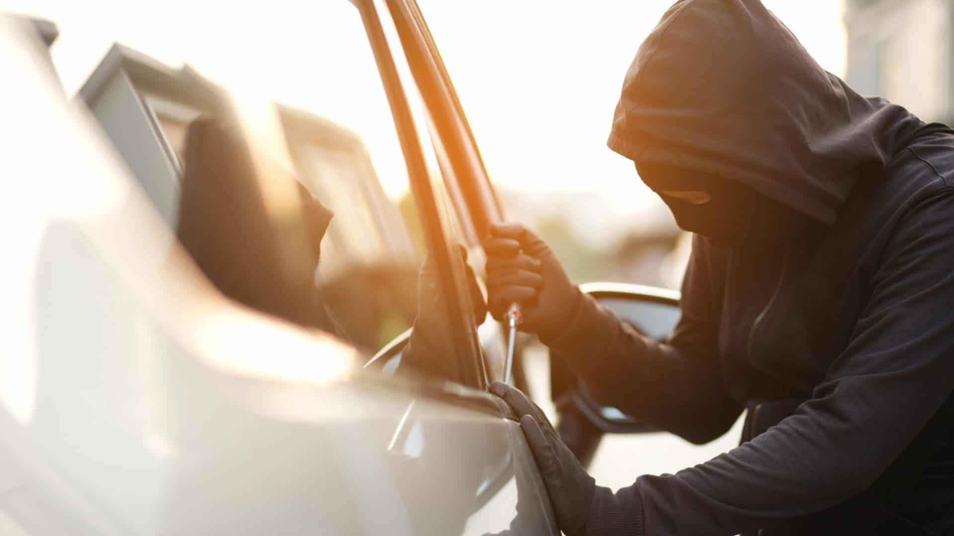 Close up de uma mão de ladrão de carros segurando uma chave de fenda, um puxador e uma luva preta roubando um automóvel,