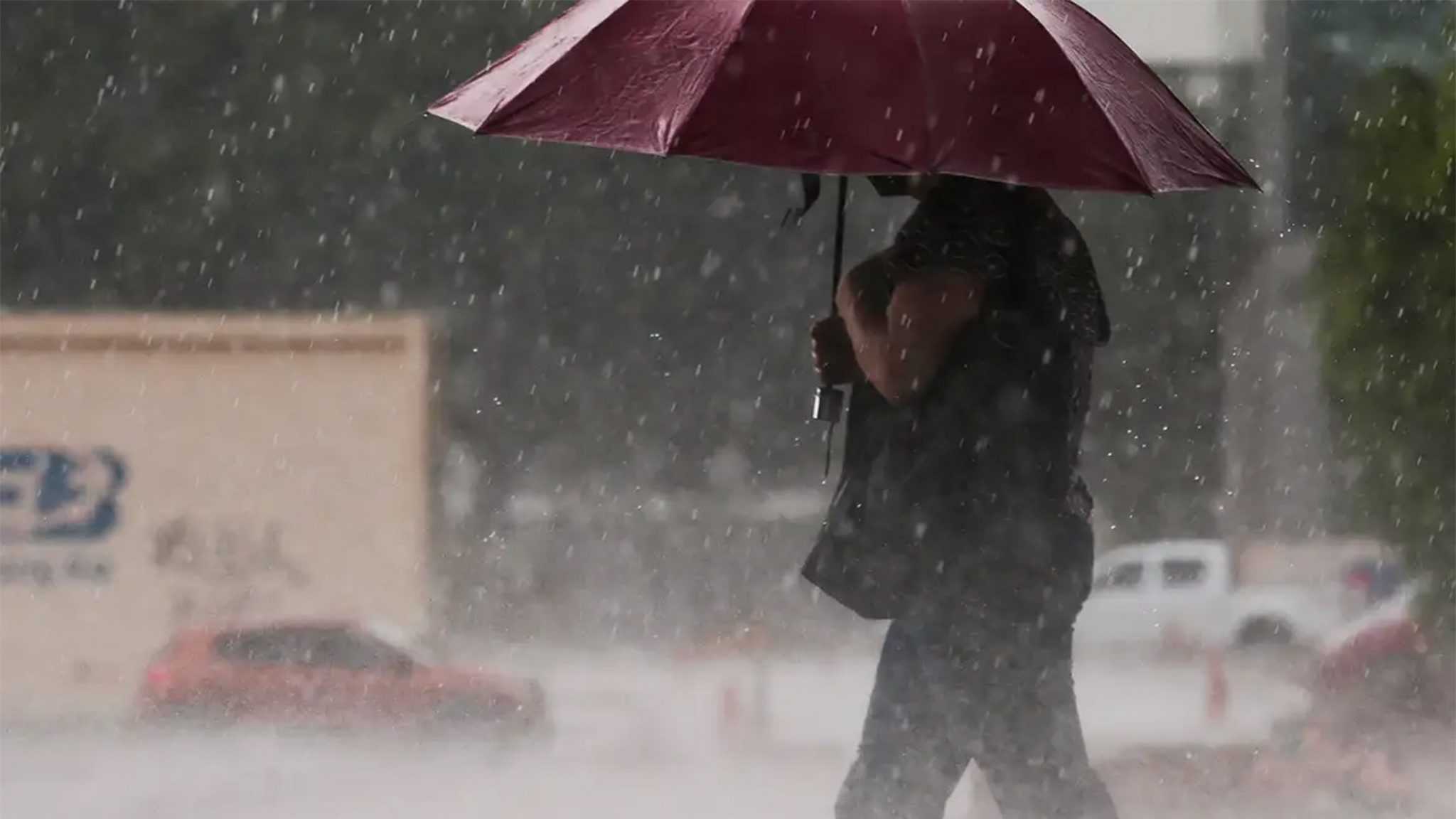 Mulher andando na rua com guarda-chuva aberto durante chuva
