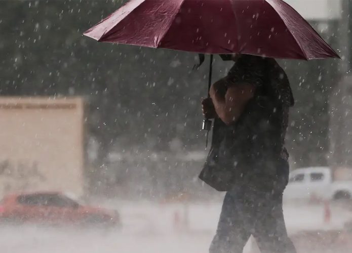 Mulher andando na rua com guarda-chuva aberto durante chuva