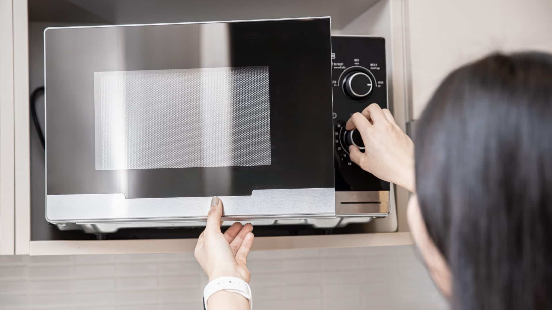 Mulher mexendo em botões no micro-ondas