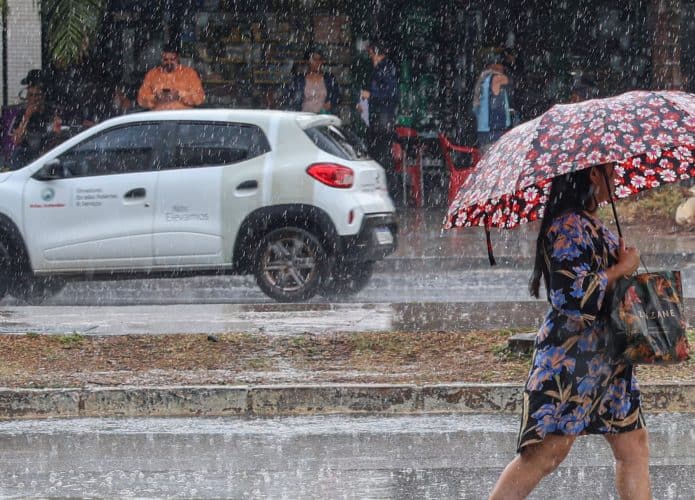 Mulher andando na chuva com guarda-chuva aberto em avenida