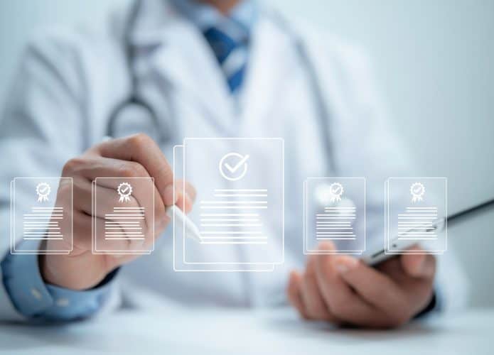 Médico com um tablet na mão e selecionando, no ar, um ícone de documento com uma caneta