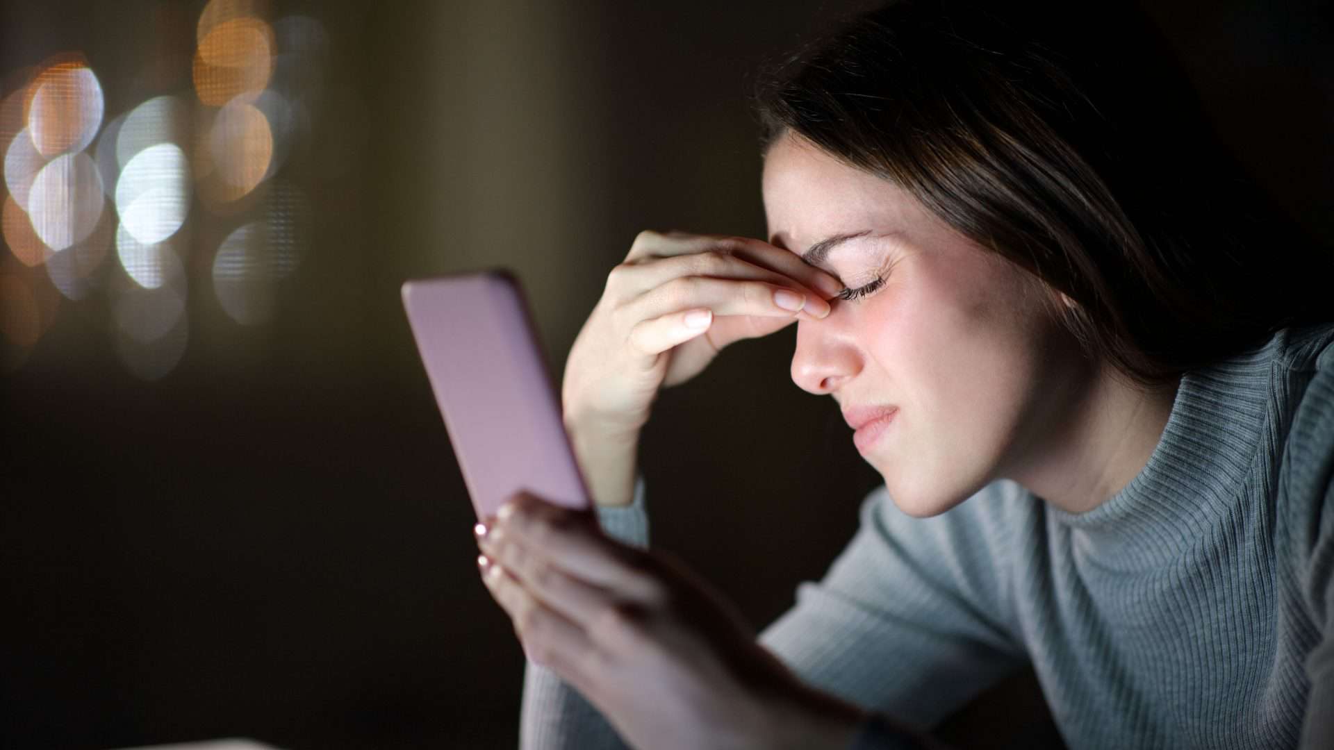 Imagem de mulher pressionando a cabeça e olhando para o celular para contextualizar se o a radiação faz mal