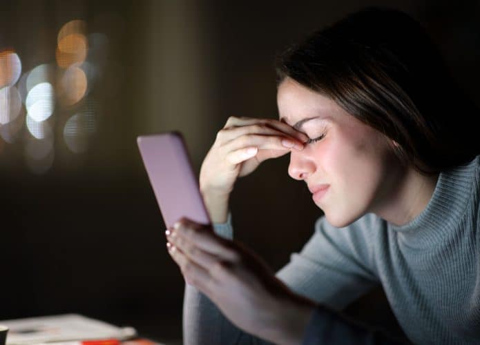 Imagem de mulher pressionando a cabeça e olhando para o celular para contextualizar se o a radiação faz mal