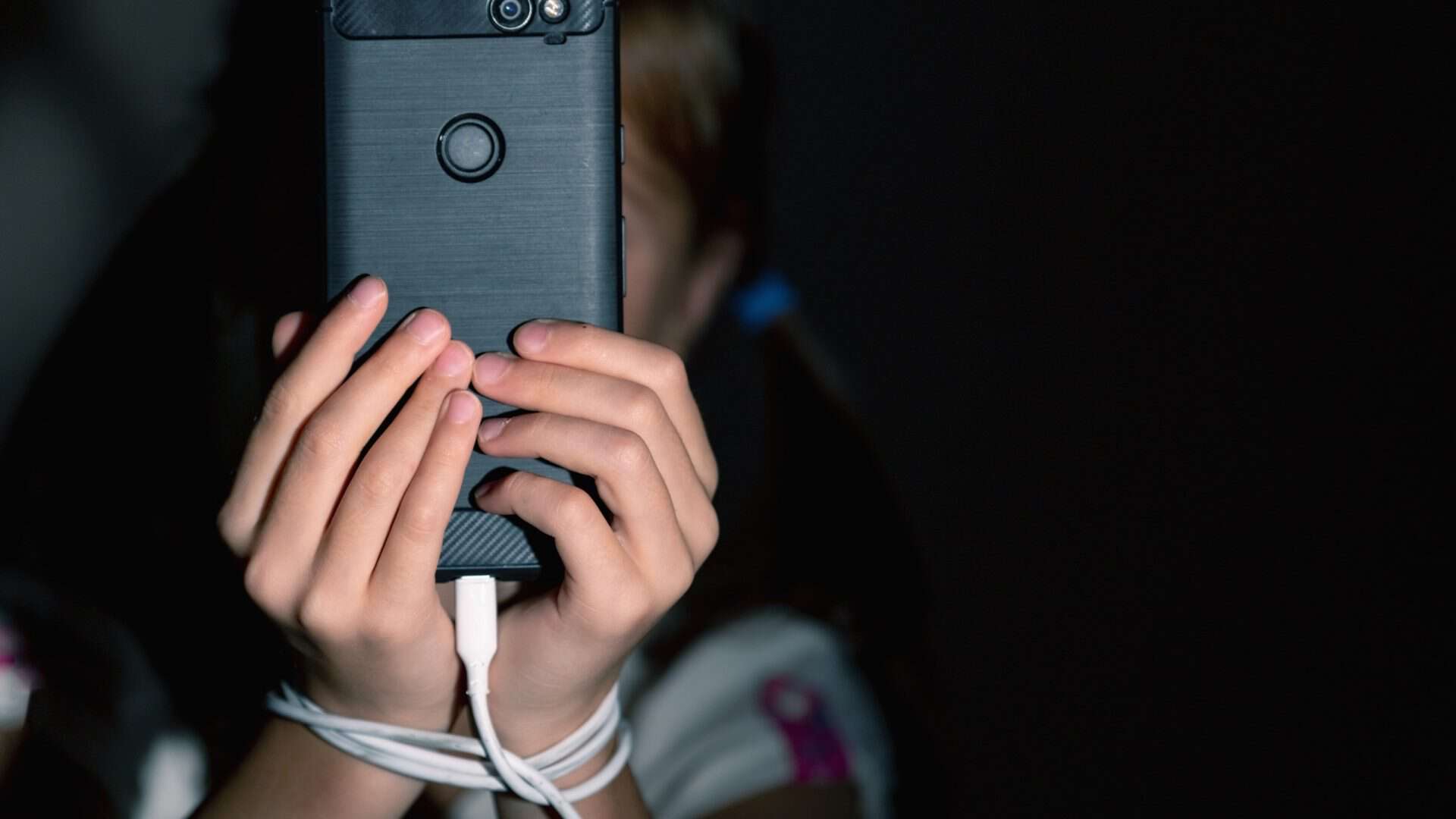 Criança usando celular e amarrada a um fone de ouvido