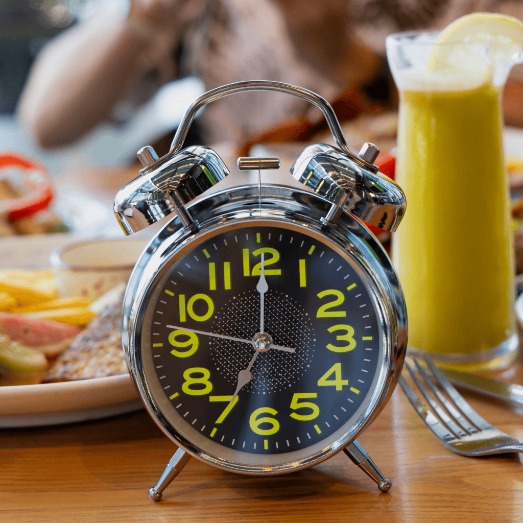 relógio antigo de mesa e atrás pessoas fazem refeição à mesa.