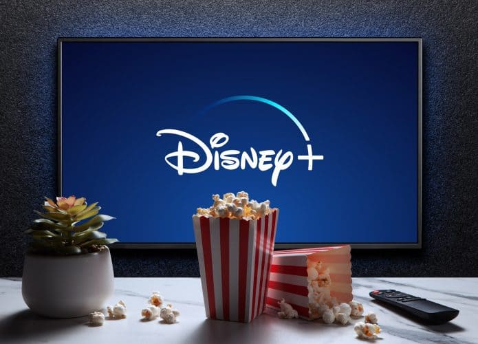 Logo do Dsney+ em uma TV; à frente, baldes de pipocas em uma mesa